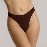 A woman wearing a brown thong on a plain background