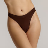 A woman wearing a brown thong on a plain background