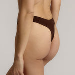 A woman wearing a brown thong on a plain background
