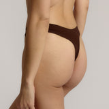 A woman wearing a brown thong on a plain background