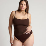 Woman wearing a brown tank top and underwear on a light gray background