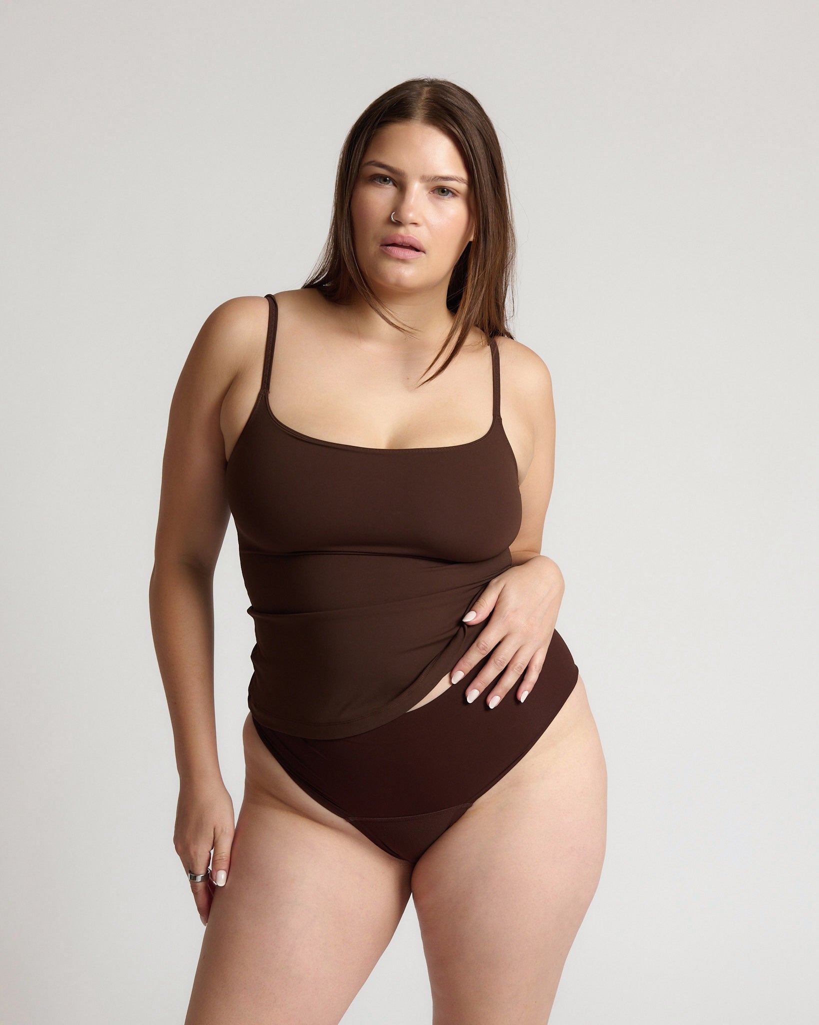Woman wearing a brown tank top and underwear on a light gray background