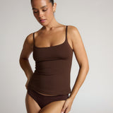 Woman wearing a brown tank top and high-waisted underwear on a plain background