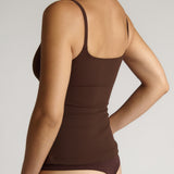 Woman wearing a brown tank top and underwear on a light gray background