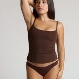 Woman wearing a brown tank top and underwear on a light gray background