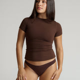 Woman wearing a brown short-sleeve top and underwear set against a plain background