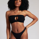 Woman wearing black strapless system against a neutral background