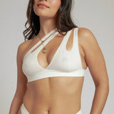 A person wearing a white, solid-colored bra and matching thong, with unique strap details and a v-neckline.
