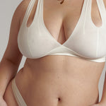 A person wearing a white, solid-colored bra and matching thong, with unique strap details and a v-neckline.