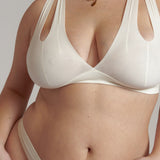 A person wearing a white, solid-colored bra and matching thong, with unique strap details and a v-neckline.