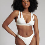 A person wearing a white, solid-colored bra and matching thong, with unique strap details and a v-neckline.