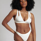 A person wearing a white, solid-colored bra and matching thong, with unique strap details and a v-neckline.