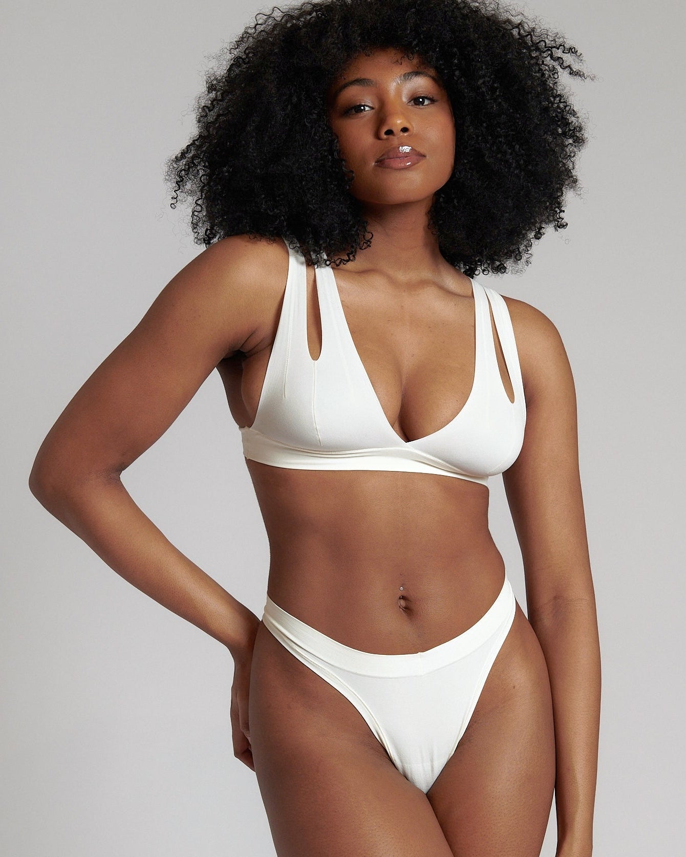 A person wearing a white, solid-colored bra and matching thong, with unique strap details and a v-neckline.