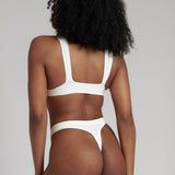 A person wearing a white, solid-colored bra and matching thong, with unique strap details and a v-neckline.