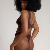 A woman wearing a brown Vii System bra, which is designed with a deep neckline, wide straps, and a smooth back.