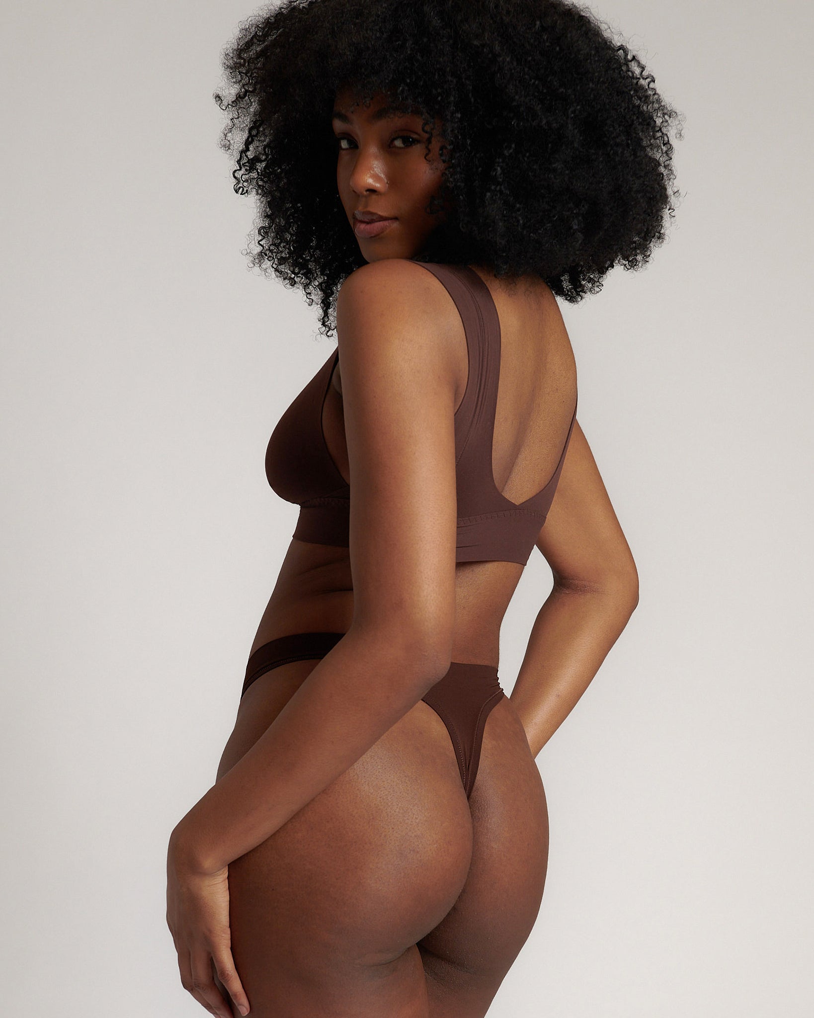 A woman wearing a brown Vii System bra, which is designed with a deep neckline, wide straps, and a smooth back.