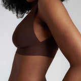 A woman wearing a brown Vii System bra, which is designed with a deep neckline, wide straps, and a smooth back.