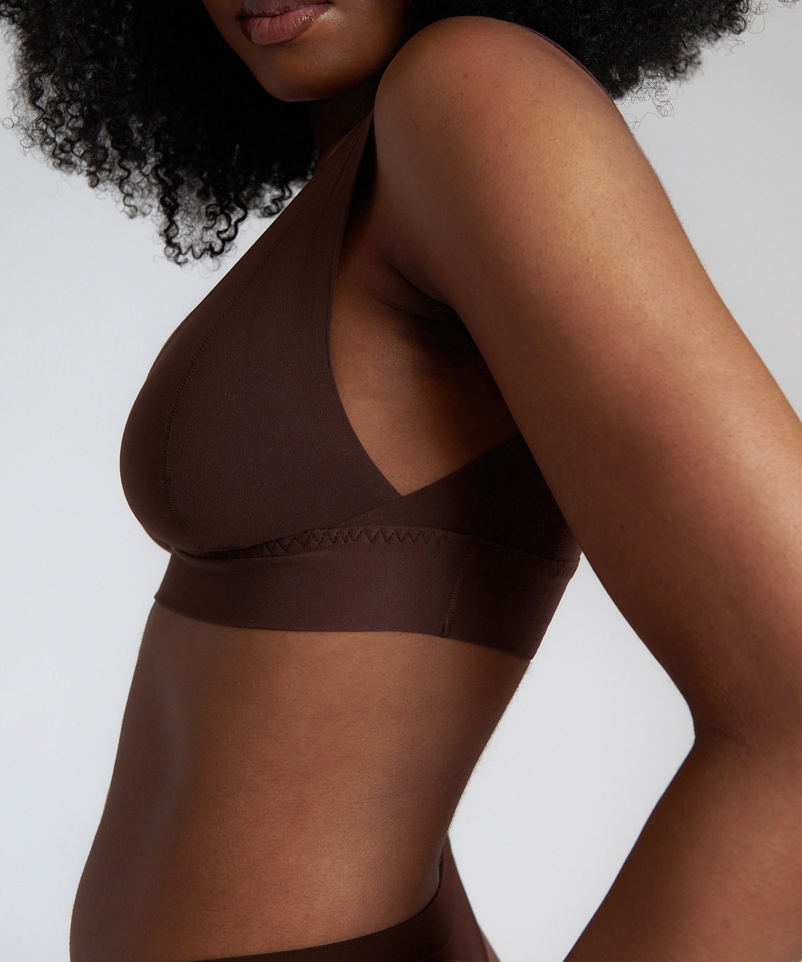 A woman wearing a brown Vii System bra, which is designed with a deep neckline, wide straps, and a smooth back.