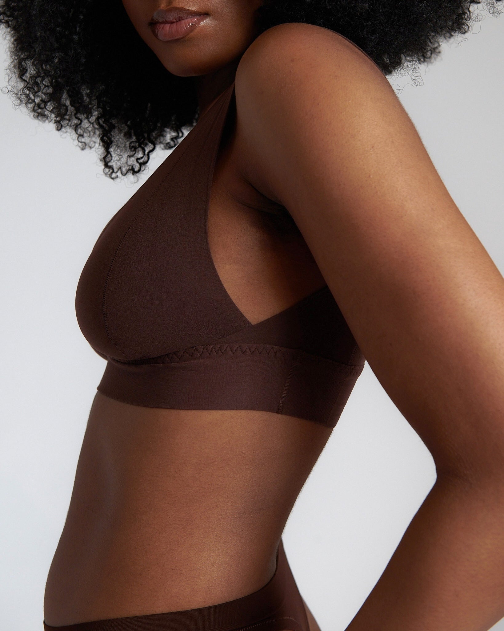 A woman wearing a brown Vii System bra, which is designed with a deep neckline, wide straps, and a smooth back.