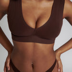 A woman wearing a brown Vii System bra, which is designed with a deep neckline, wide straps, and a smooth back.