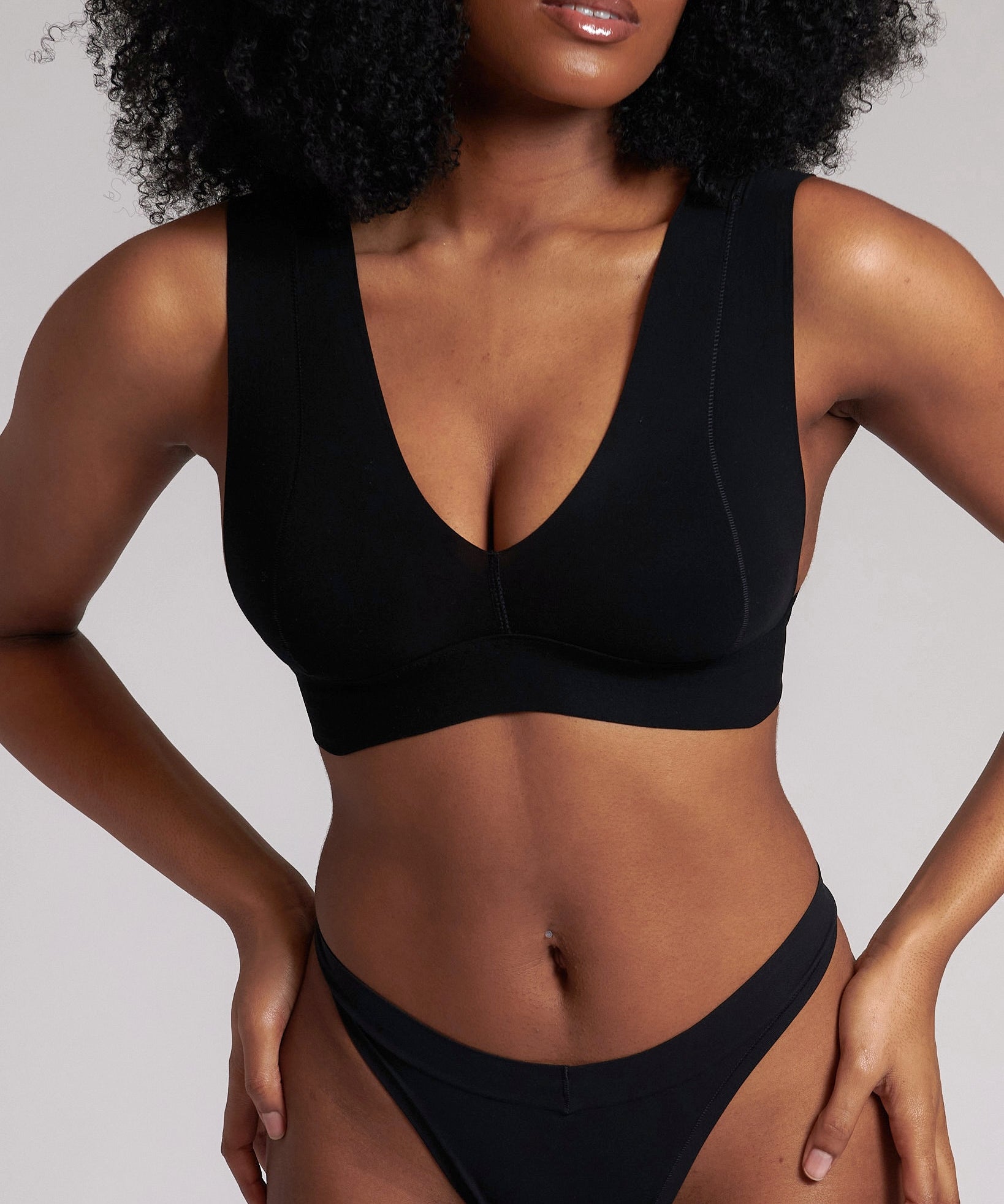 A woman wearing a black minimalist bra with wide straps and a deep neckline.