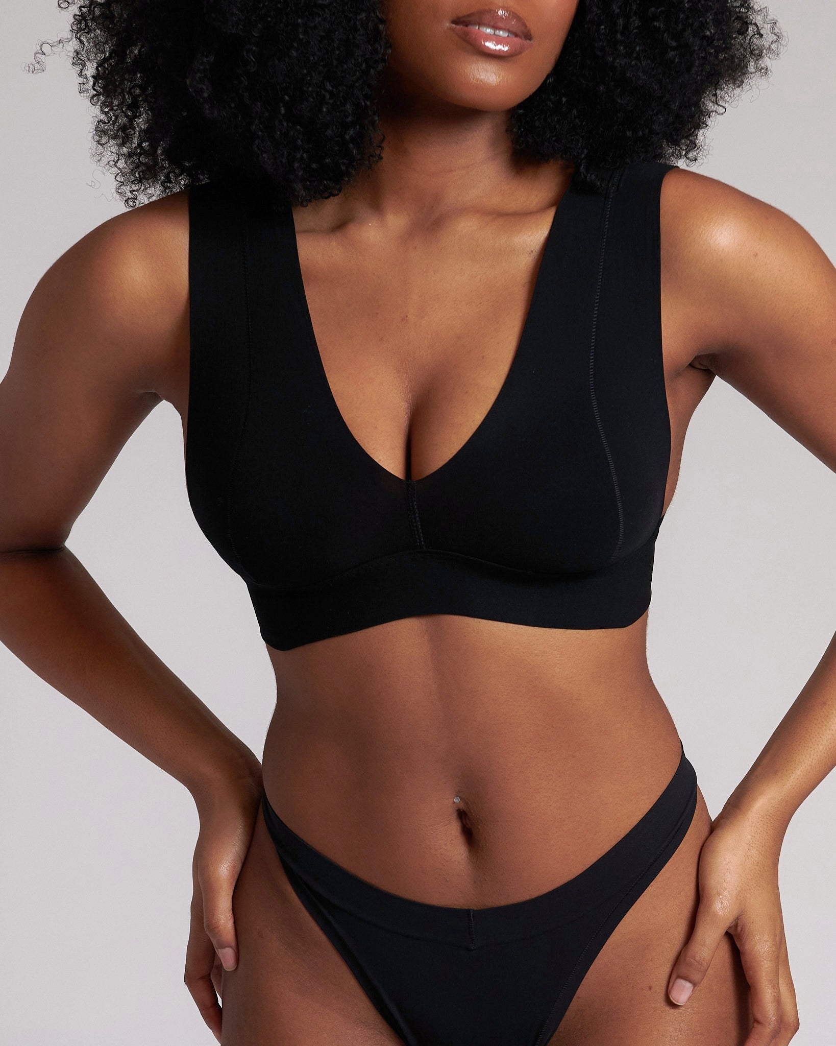 A woman wearing a black minimalist bra with wide straps and a deep neckline.