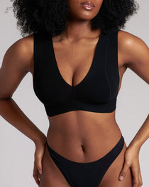 A woman wearing a black minimalist bra with wide straps and a deep neckline.