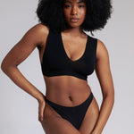 A woman wearing a black minimalist bra with wide straps and a deep neckline.