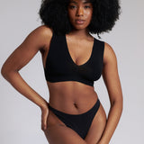 A woman wearing a black minimalist bra with wide straps and a deep neckline.