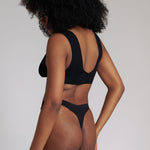 A woman wearing a black minimalist bra with wide straps and a deep neckline.