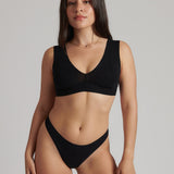 A woman wearing a black minimalist bra with wide straps and a deep neckline.