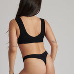 A woman wearing a black minimalist bra with wide straps and a deep neckline.