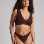 A woman wearing a brown Vii System bra, which is designed with a deep neckline, wide straps, and a smooth back.