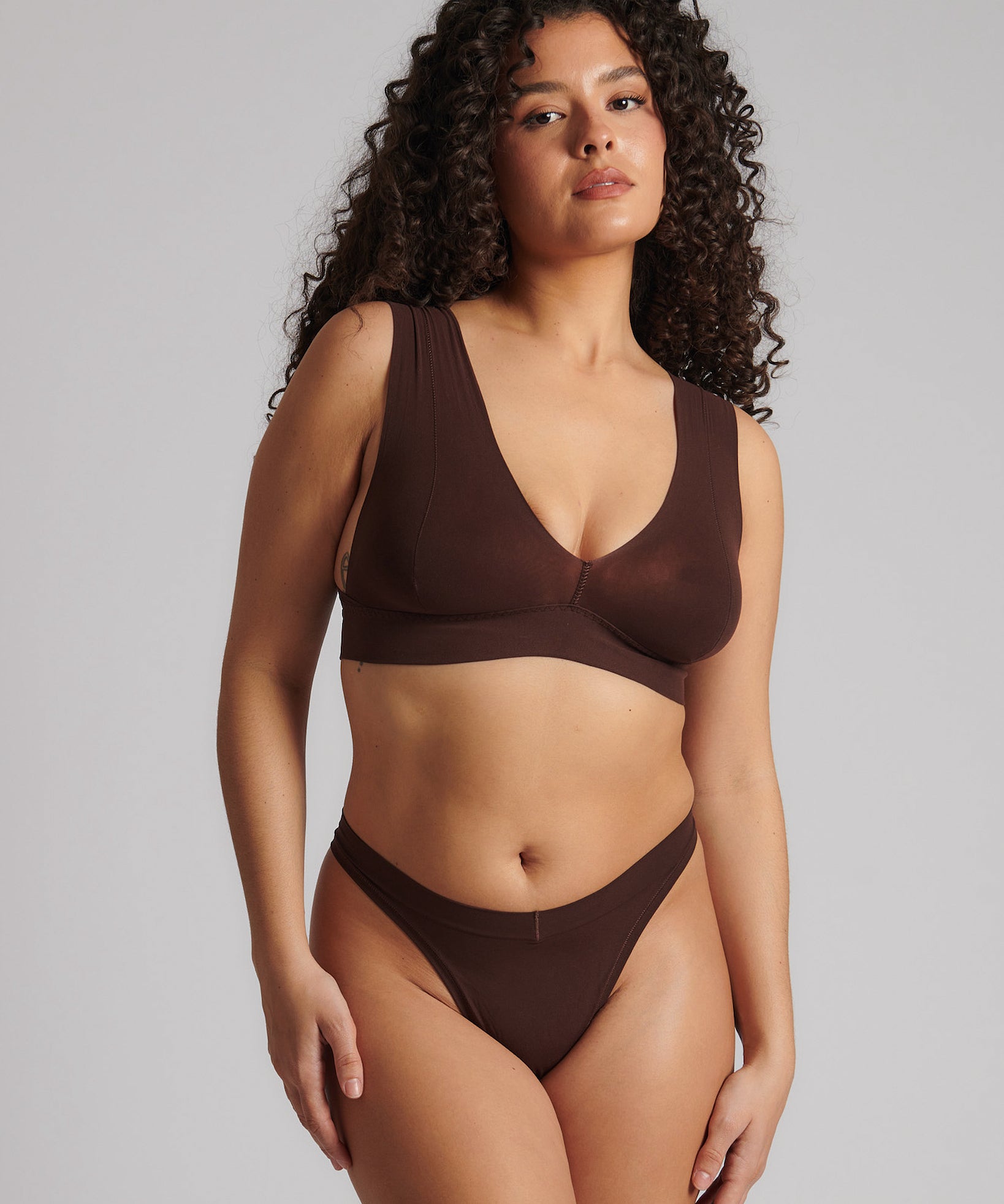 A woman wearing a brown Vii System bra, which is designed with a deep neckline, wide straps, and a smooth back.