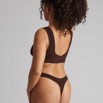 A woman wearing a brown Vii System bra, which is designed with a deep neckline, wide straps, and a smooth back.