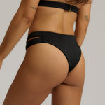 Person wearing black high-waisted bikini bottoms on a neutral background