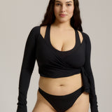 Woman wearing a black wrap top and black thong on a plain background