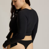 Woman wearing a black wrap top and black thong on a plain background