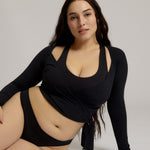 Woman wearing a black wrap top and black thong on a plain background