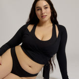 Woman wearing a black wrap top and black thong on a plain background
