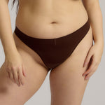 A woman wearing a brown thong on a plain background