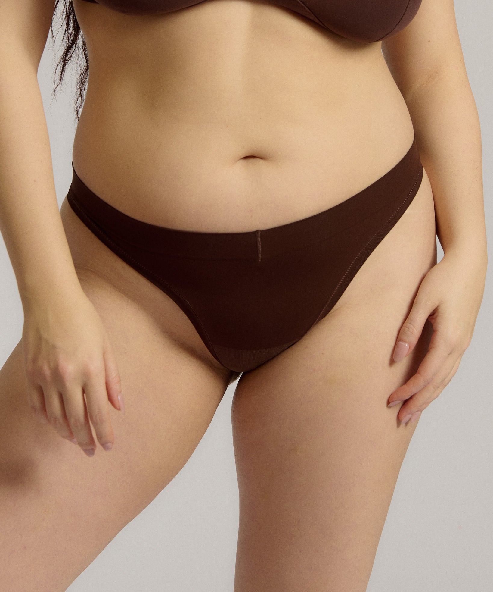 A woman wearing a brown thong on a plain background