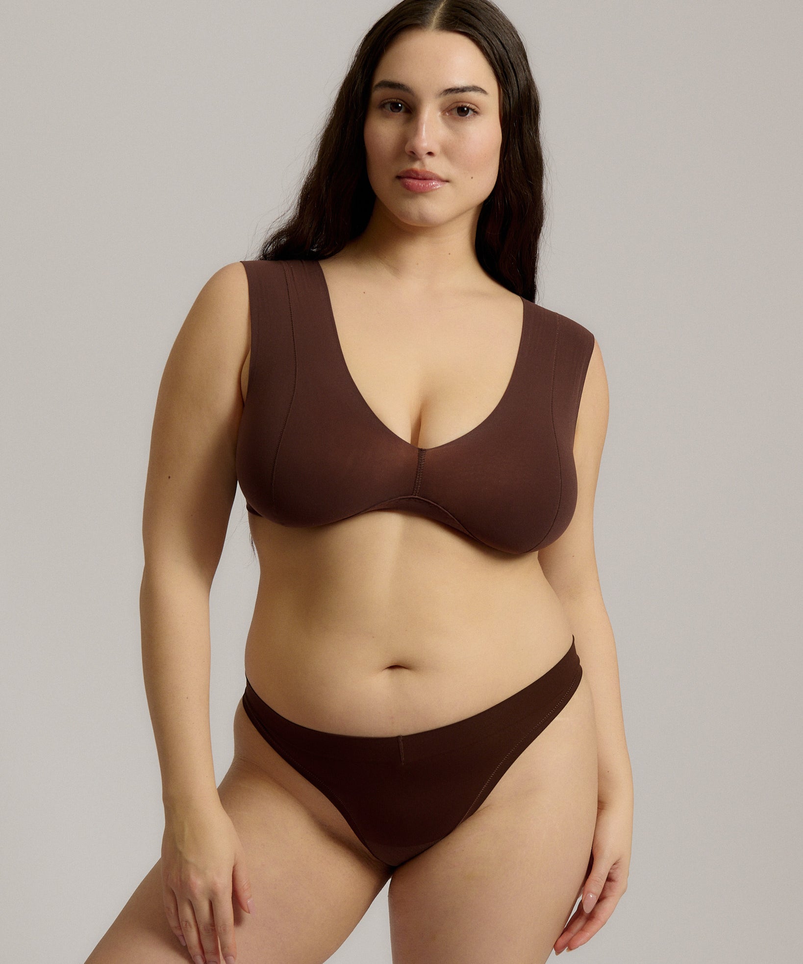 A woman wearing a brown Vii System bra, which is designed with a deep neckline, wide straps, and a smooth back.