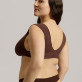 A woman wearing a brown Vii System bra, which is designed with a deep neckline, wide straps, and a smooth back.