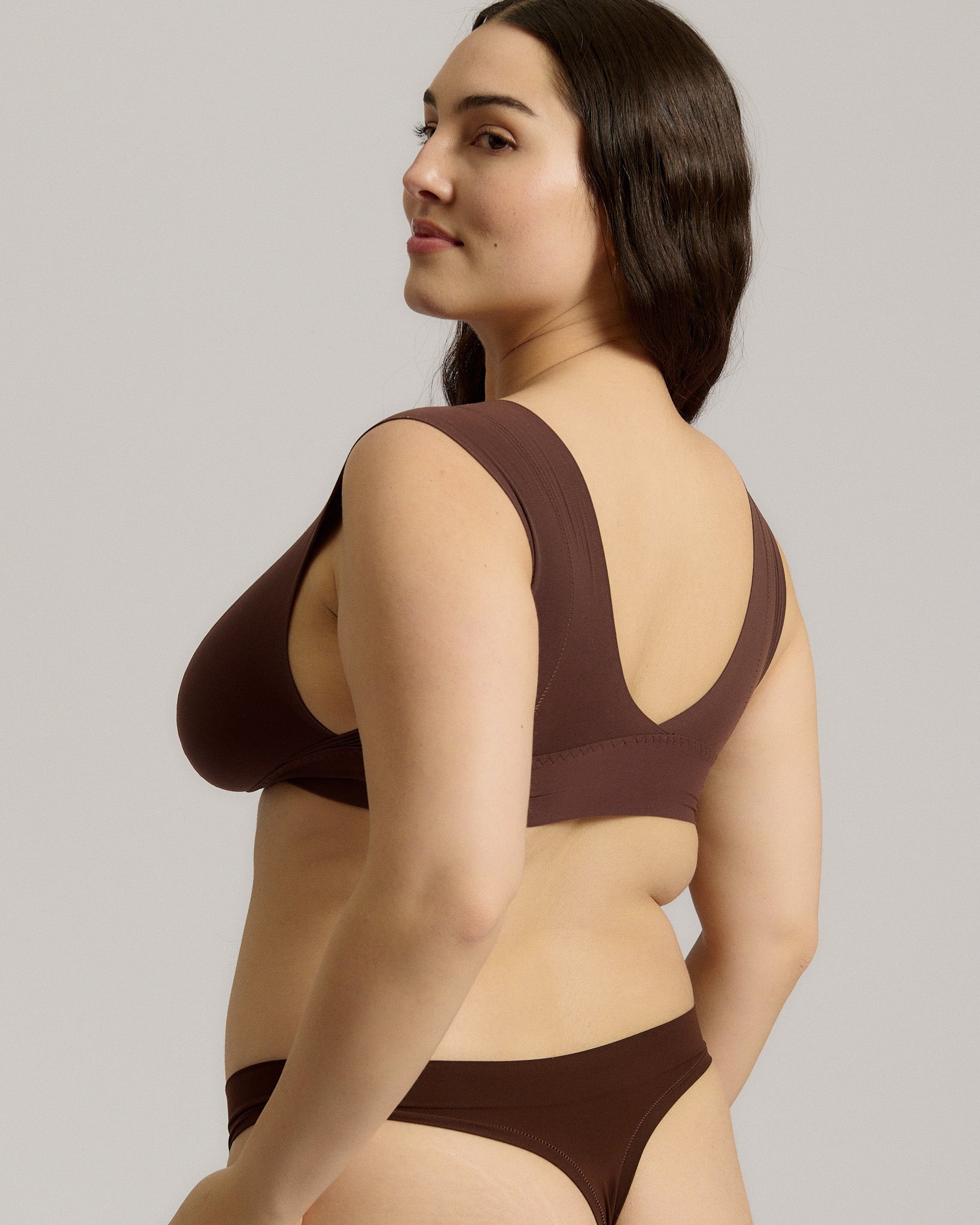 A woman wearing a brown Vii System bra, which is designed with a deep neckline, wide straps, and a smooth back.