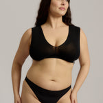 A woman wearing a black minimalist bra with wide straps and a deep neckline.