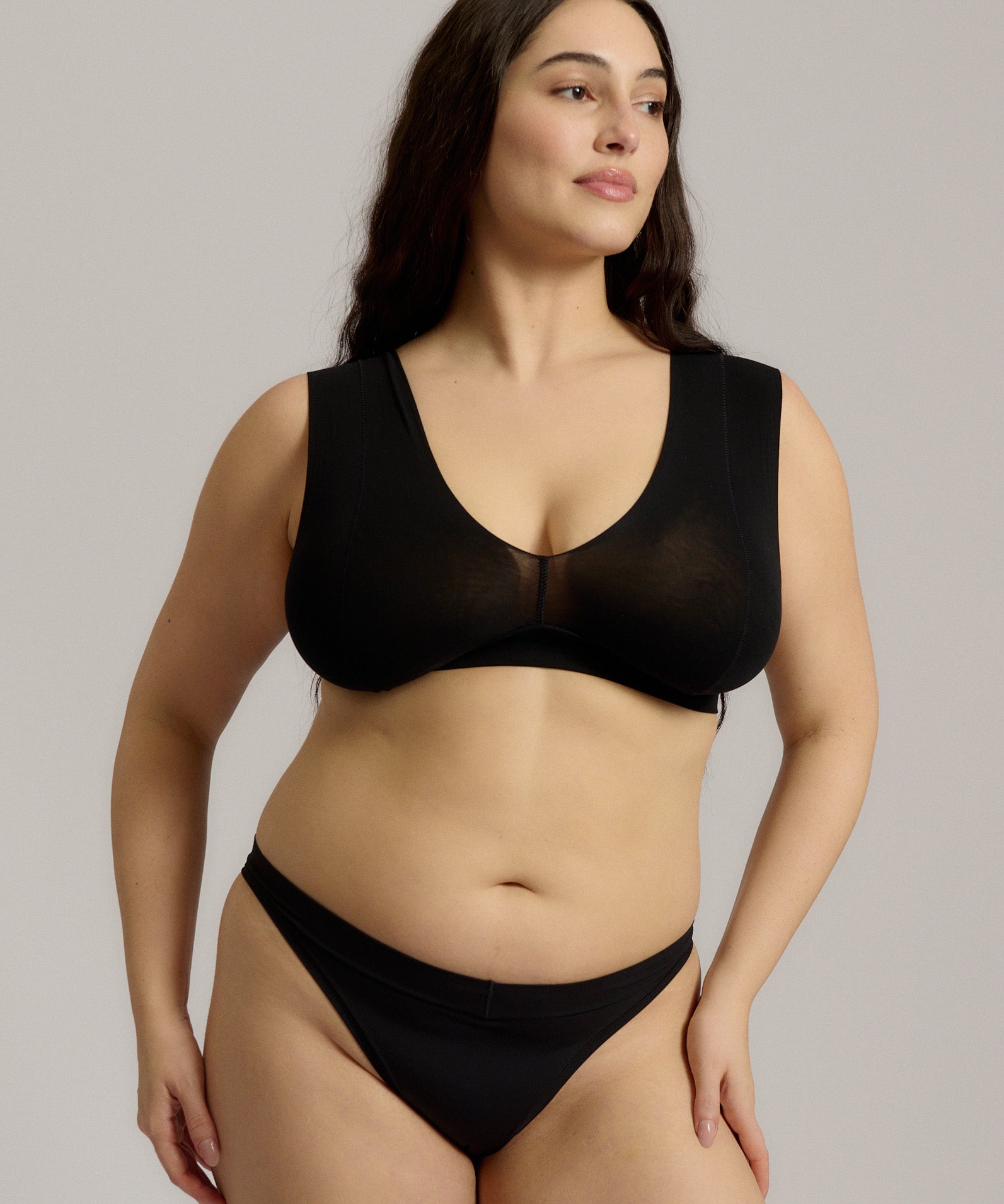 A woman wearing a black minimalist bra with wide straps and a deep neckline.