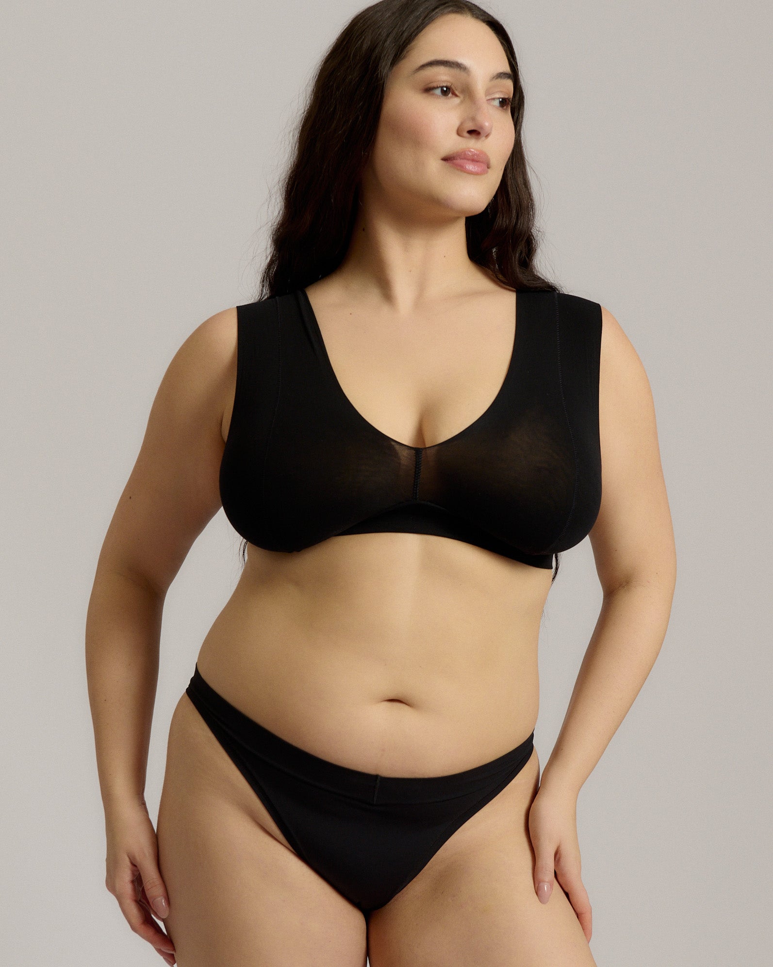 A woman wearing a black minimalist bra with wide straps and a deep neckline.