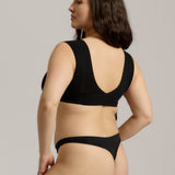 A woman wearing a black minimalist bra with wide straps and a deep neckline.