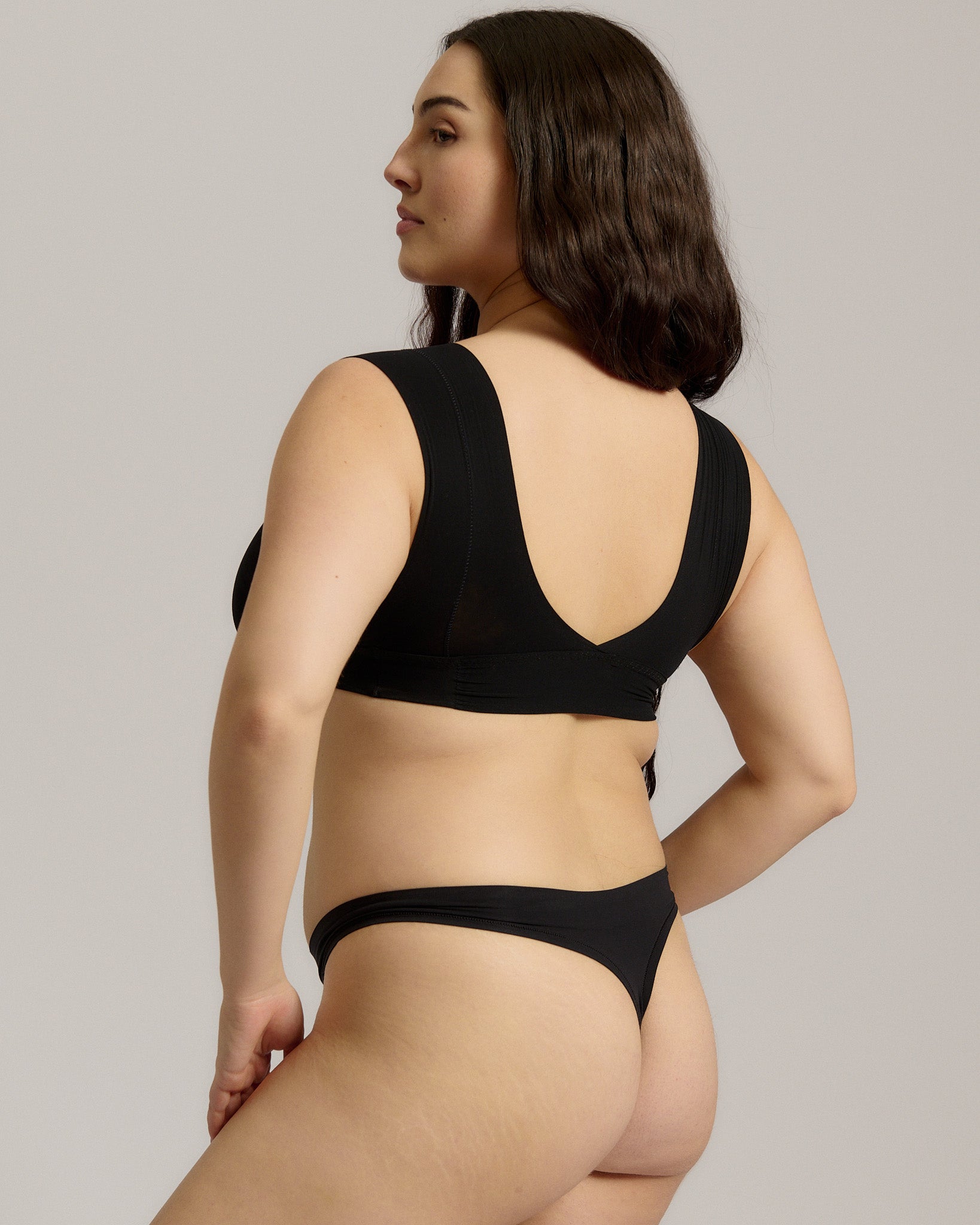 A woman wearing a black minimalist bra with wide straps and a deep neckline.